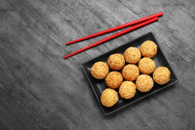 Photo of Delicious sesame balls and chopsticks on black table, top view. Space for text