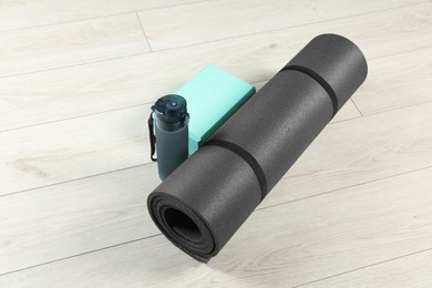 Photo of Exercise mat, yoga block and bottle of water on light wooden floor