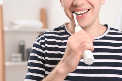 Photo of Man brushing his teeth with electric toothbrush in bathroom, closeup