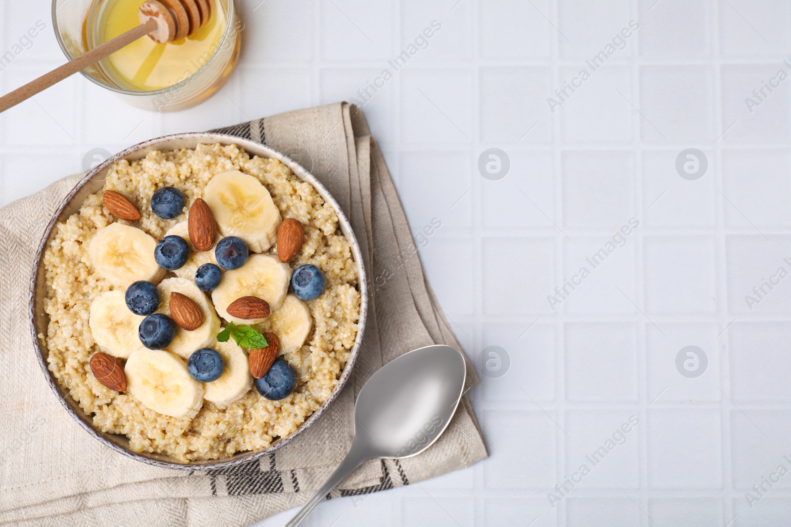 Photo of Bowl of delicious cooked quinoa with almonds, bananas and blueberries on white table, flat lay. Space for text