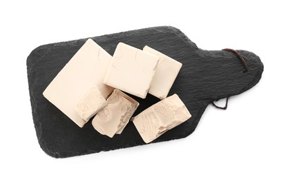 Slate board with pieces of compressed yeast on white background, top view