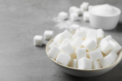 Photo of Refined sugar cubes in bowl on grey table