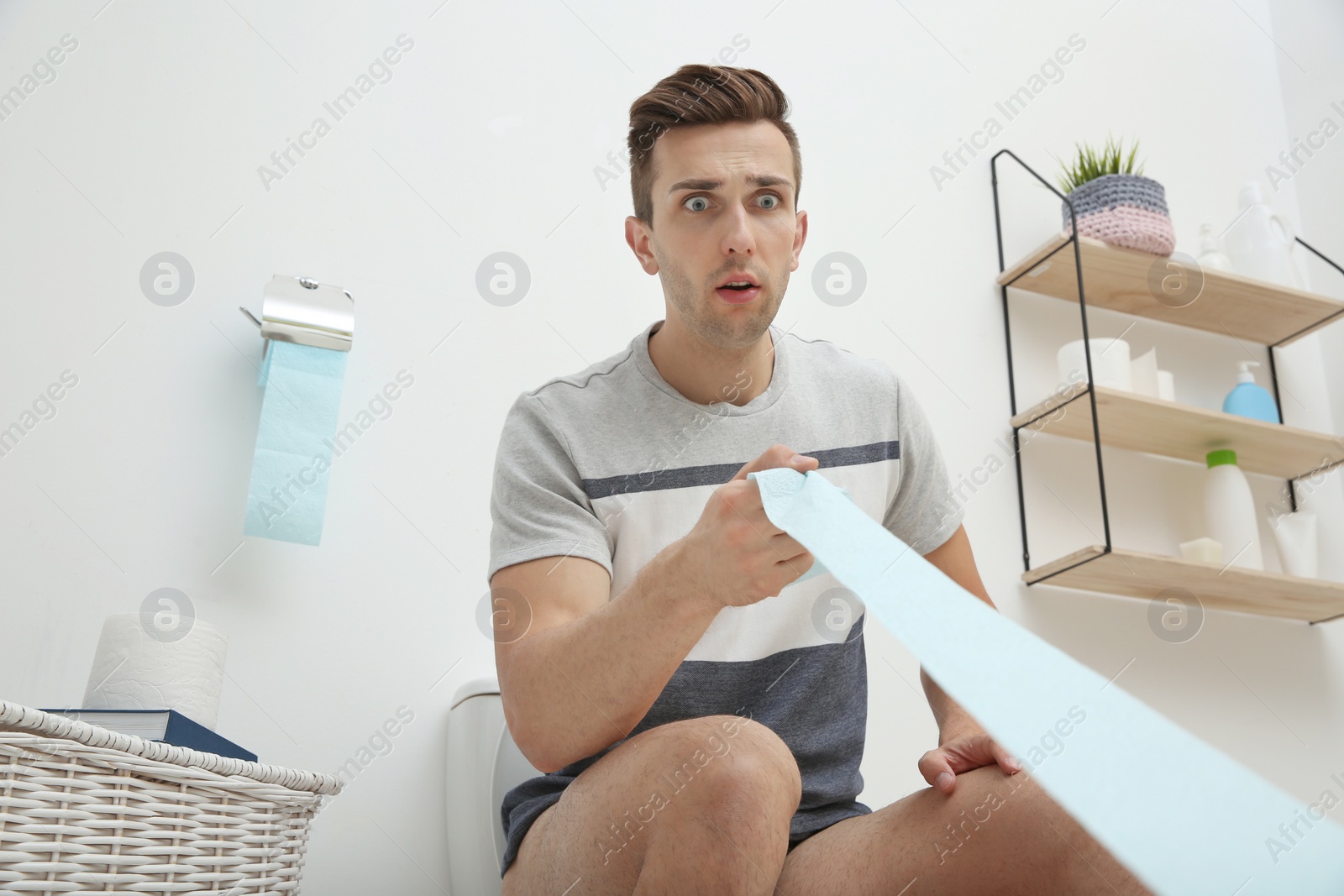 Photo of Young man pulling toilet paper in bathroom