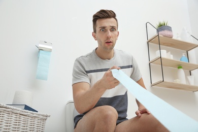 Young man pulling toilet paper in bathroom