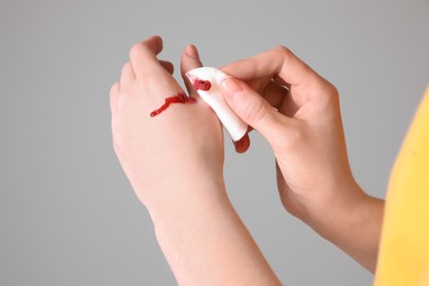 Photo of Woman wiping cut finger with cotton pad on grey background, closeup