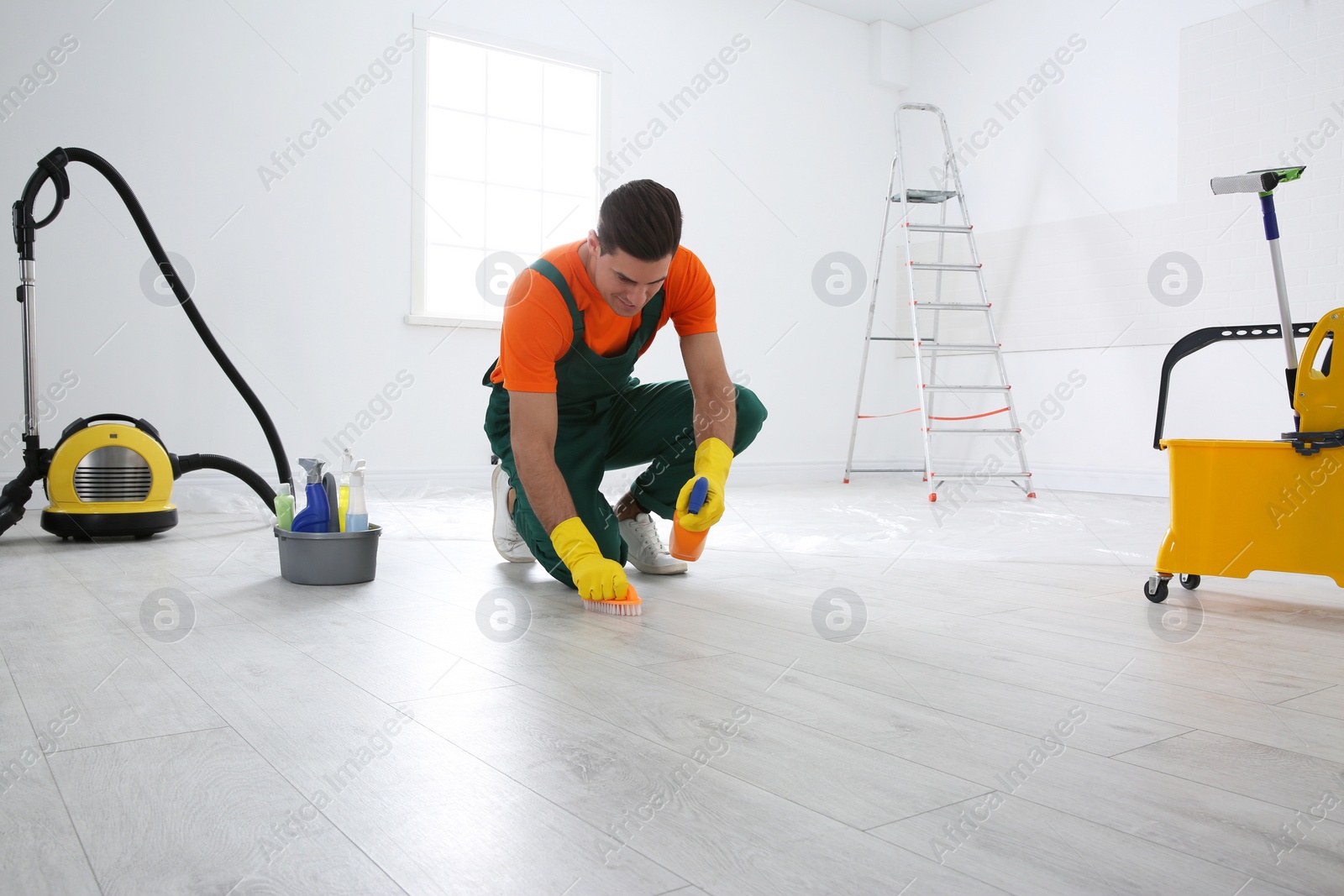 Photo of Professional janitor cleaning floor with brush and detergent after renovation