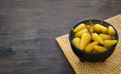 Photo of Bowl of pickled yellow jalapeno peppers on wooden table. Space for text