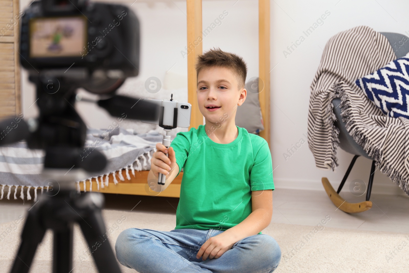 Photo of Cute little blogger with phone and selfie stick recording video at home