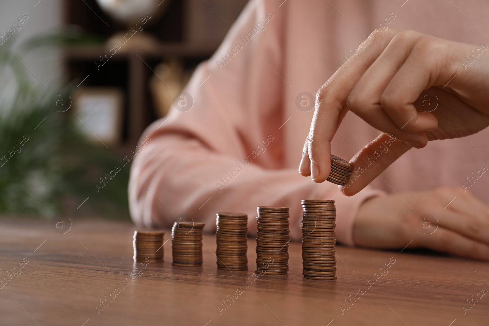 Photo of Woman stacking coins at wooden table indoors, closeup