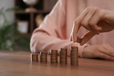 Woman stacking coins at wooden table indoors, closeup