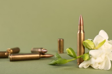 Bullets, cartridge cases and beautiful freesia flowers on olive background, space for text
