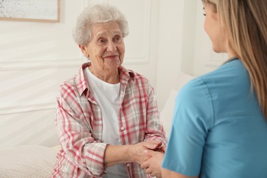 Photo of Young caregiver talking to senior woman in room. Home health care service