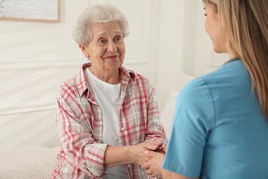 Young caregiver talking to senior woman in room. Home health care service