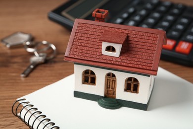 Photo of Mortgage concept. House model, notebook and calculator on wooden table, closeup