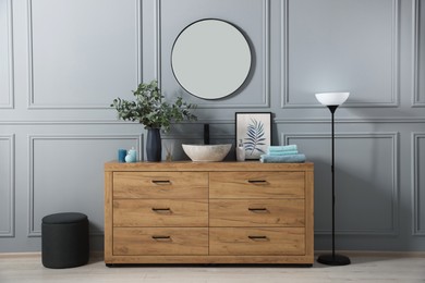 Modern bathroom interior with stylish mirror, eucalyptus branches, vessel sink and wooden vanity