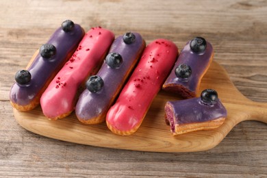 Photo of Different tasty glazed eclairs on wooden table, closeup