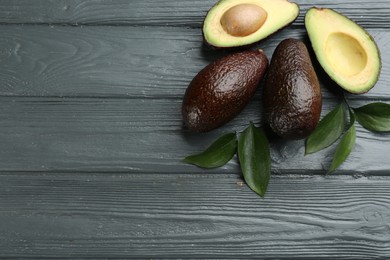 Photo of Whole and cut avocados with green leaves on grey wooden table, flat lay. Space for text