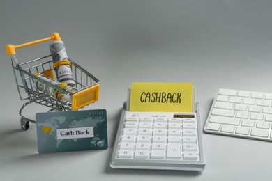 Photo of Calculator, keyboard, credit card and dollar banknotes in shopping cart on light grey background. Cashback concept