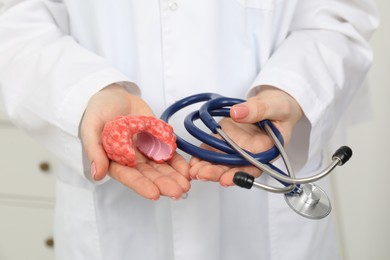 Endocrinologist holding stethoscope and model of thyroid gland, closeup