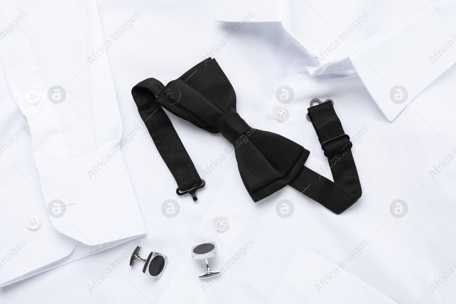 Photo of Stylish black bow tie and cufflinks on white shirt, top view