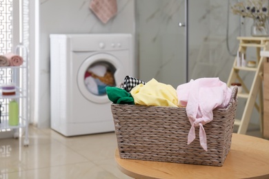 Photo of Wicker laundry basket full of different clothes on table in bathroom