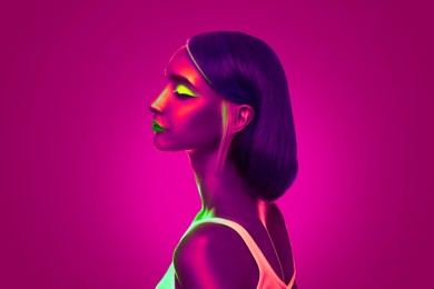 Young woman with bright makeup posing in neon lights against pink background