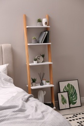 Stylish bedroom interior with decorative ladder and plants near grey wall