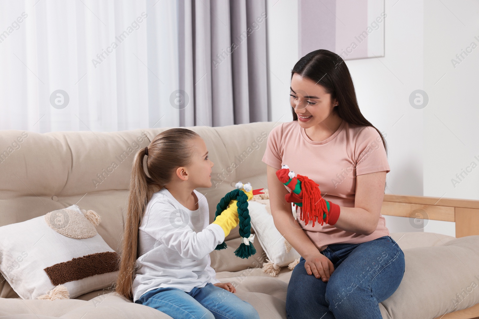 Photo of Happy mother and daughter playing with funny sock puppets together at home