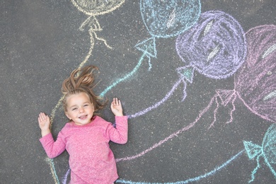 Photo of Little child lying near chalk drawing of balloons on asphalt, top view