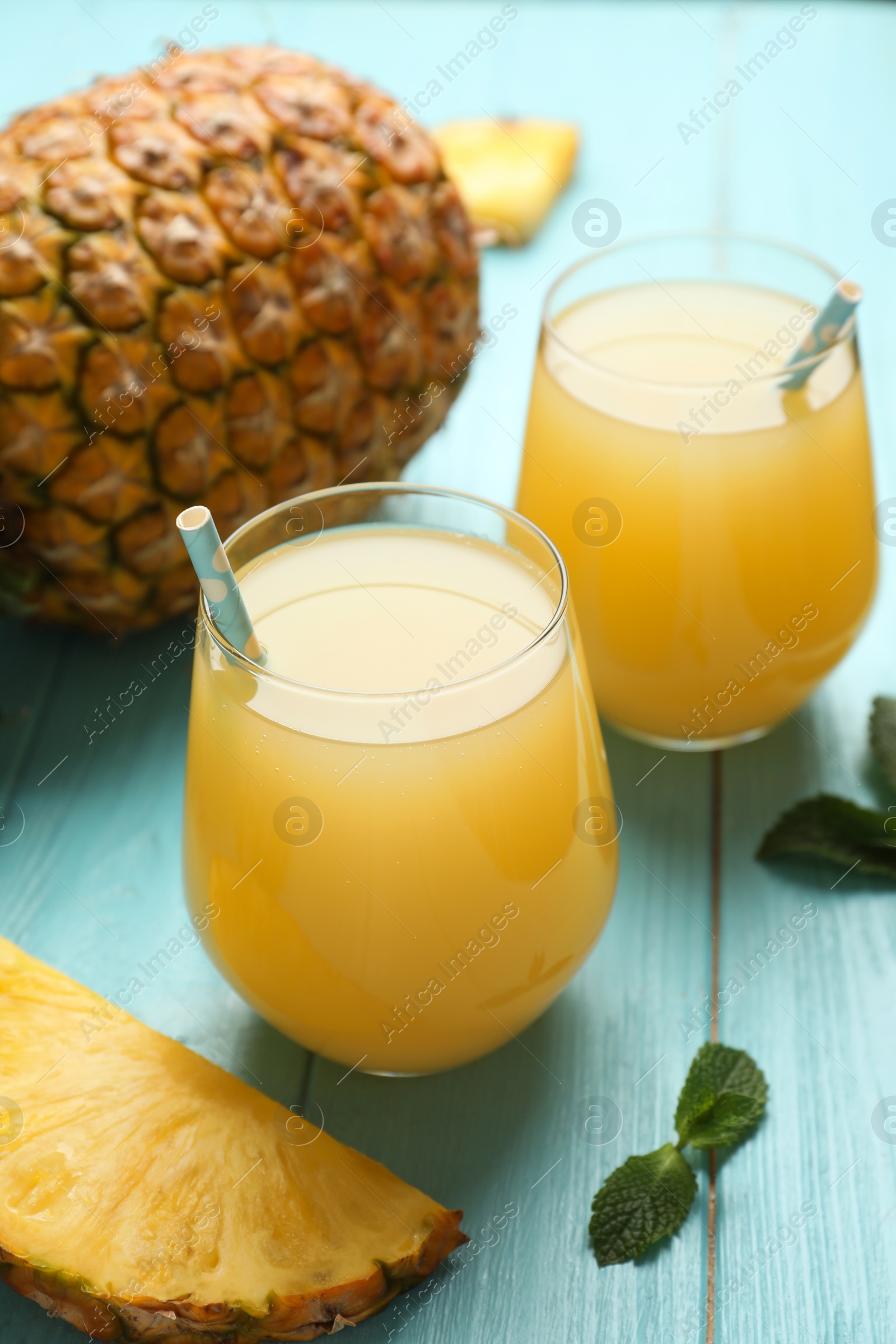 Photo of Delicious pineapple juice and fresh fruit on light blue wooden table