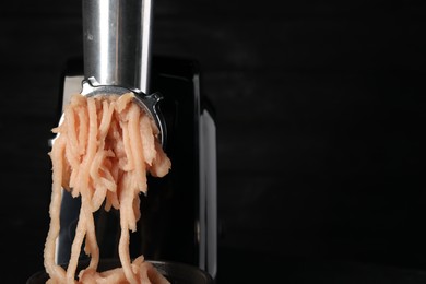 Photo of Electric meat grinder with chicken mince on black background, closeup. Space for text