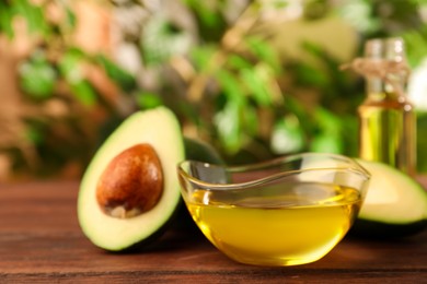 Photo of Glass bowlcooking oil and fresh avocados on wooden table against blurred green background