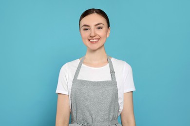 Beautiful young woman in clean apron with pattern on light blue background