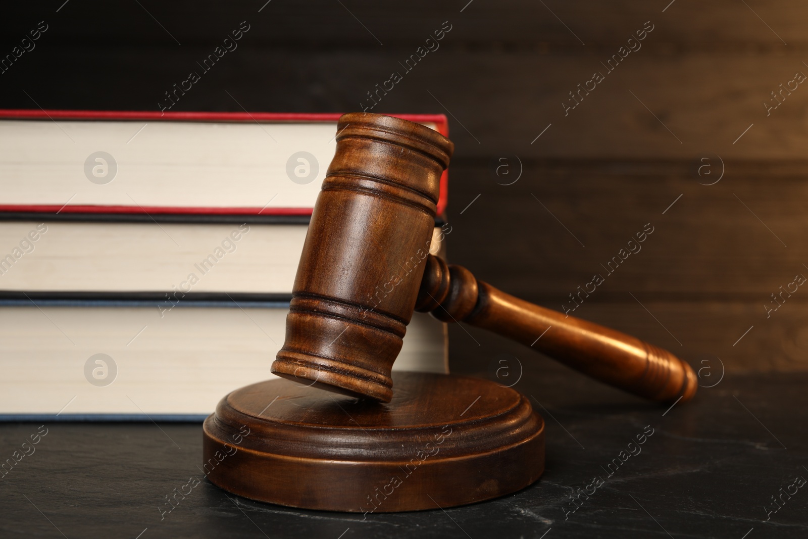 Photo of Wooden gavel and stack of books on dark textured table, closeup