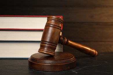 Wooden gavel and stack of books on dark textured table, closeup