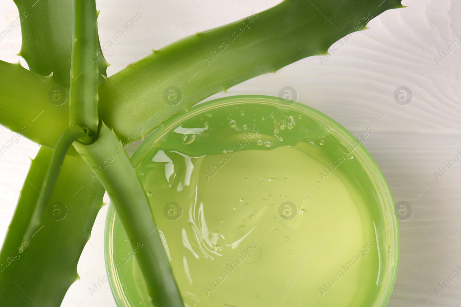 Photo of Jar of cosmetic gel and aloe vera leaves on white wooden table, top view