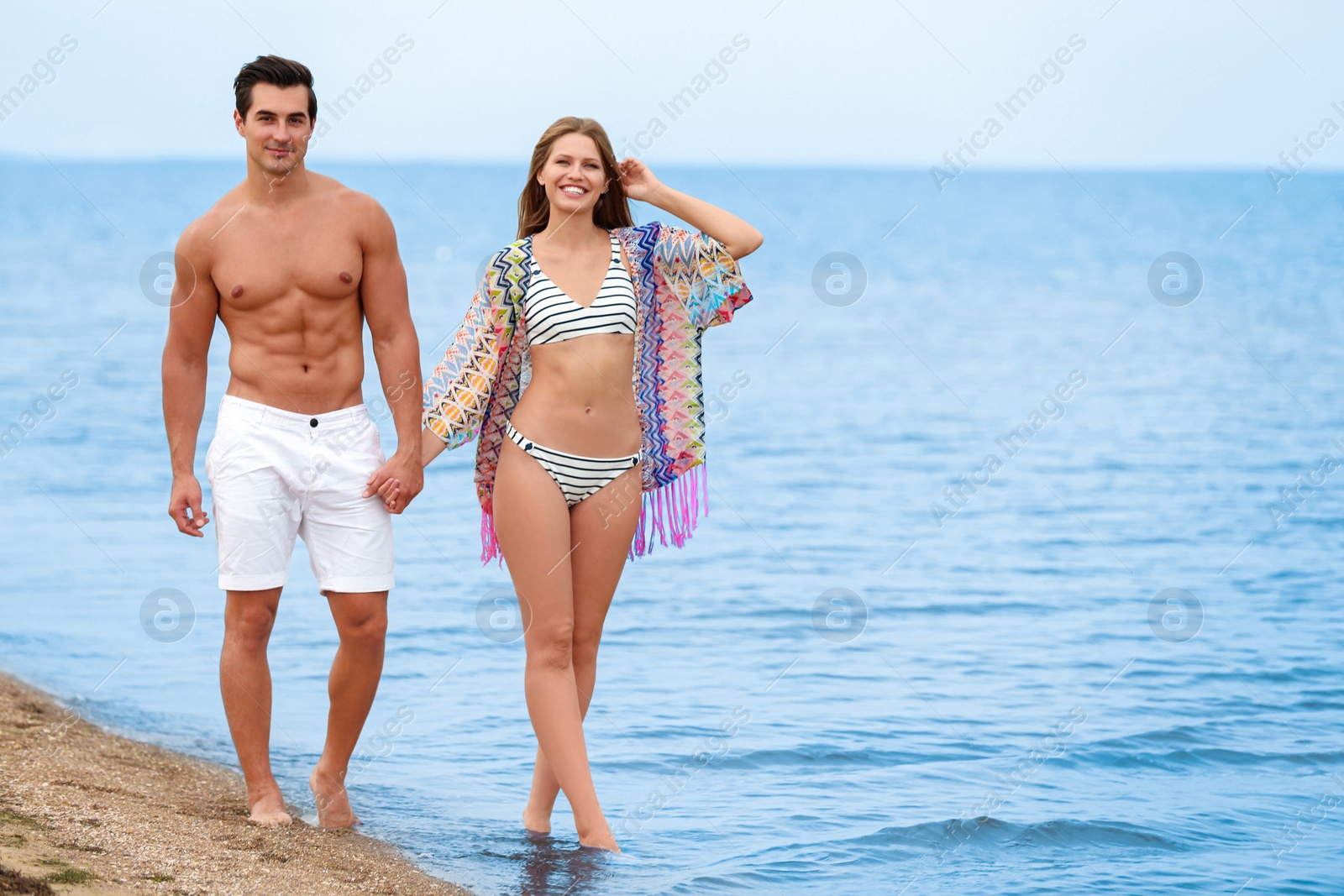 Photo of Happy young couple walking together on sea beach. Space for text