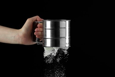 Woman sieving flour against black background, closeup. Space for text