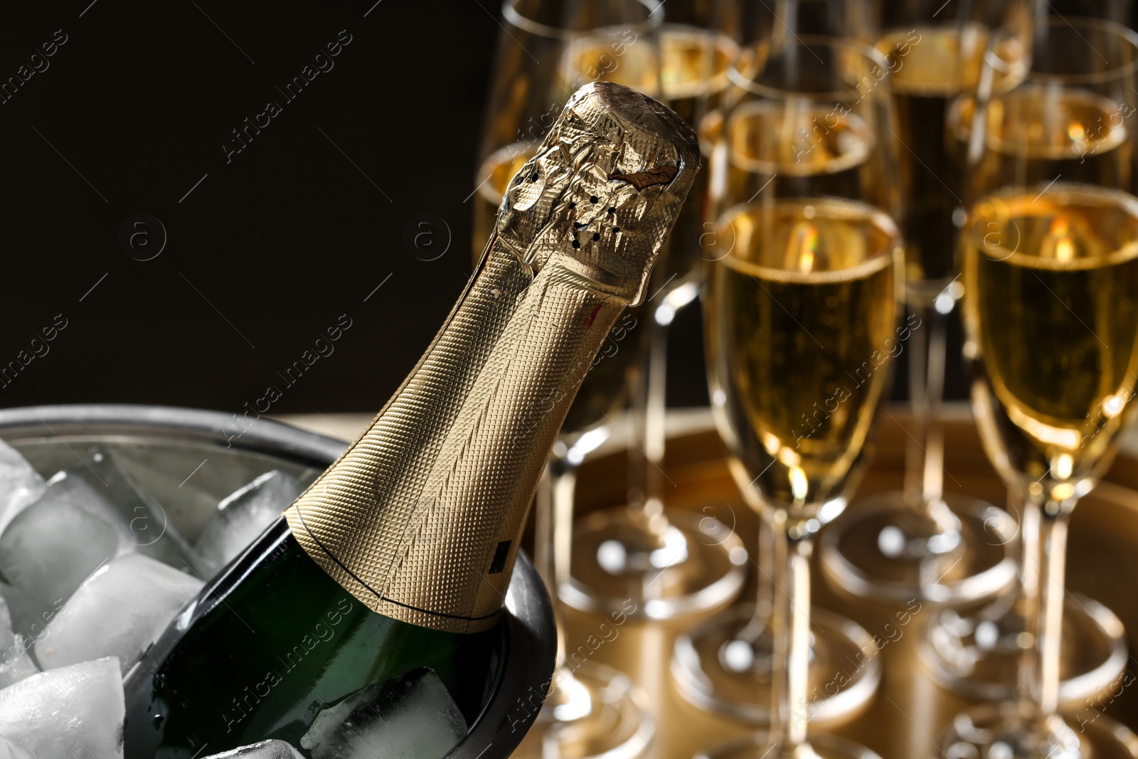 Photo of Bottle of champagne in bucket with ice and glasses on table, closeup. Space for text