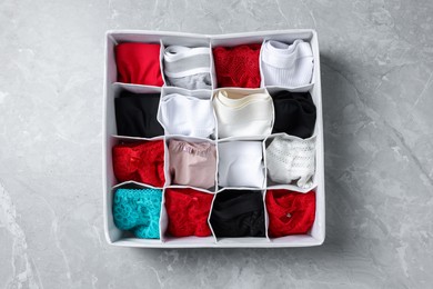 Photo of Organizer with folded women's underwear on light grey marble table, top view