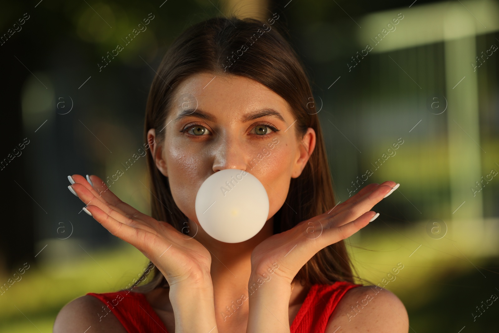 Photo of Beautiful young woman blowing bubble gum outdoors