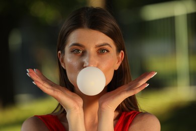 Photo of Beautiful young woman blowing bubble gum outdoors