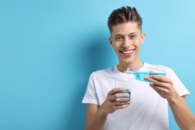 Photo of Young man using mouthwash on light blue background, space for text