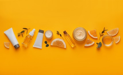 Body cream and other cosmetic products with ingredients on orange background, flat lay