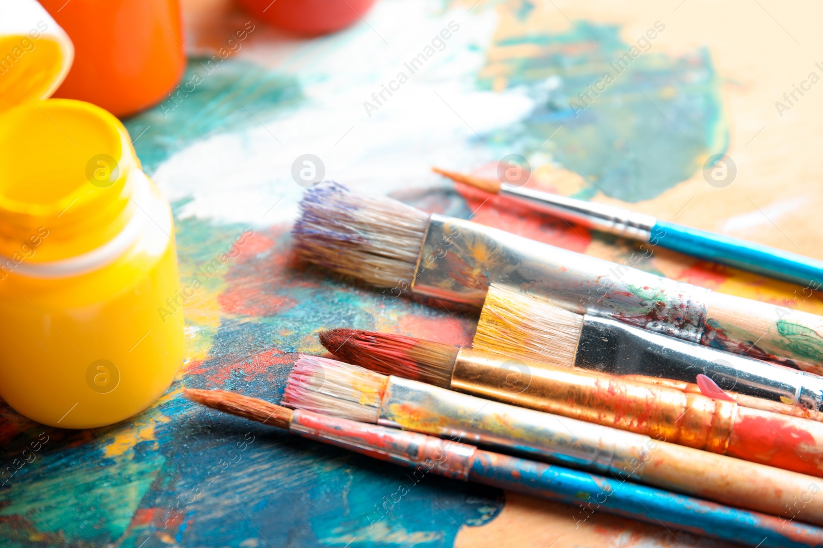 Photo of Different brushes and jars with paint on palette, closeup