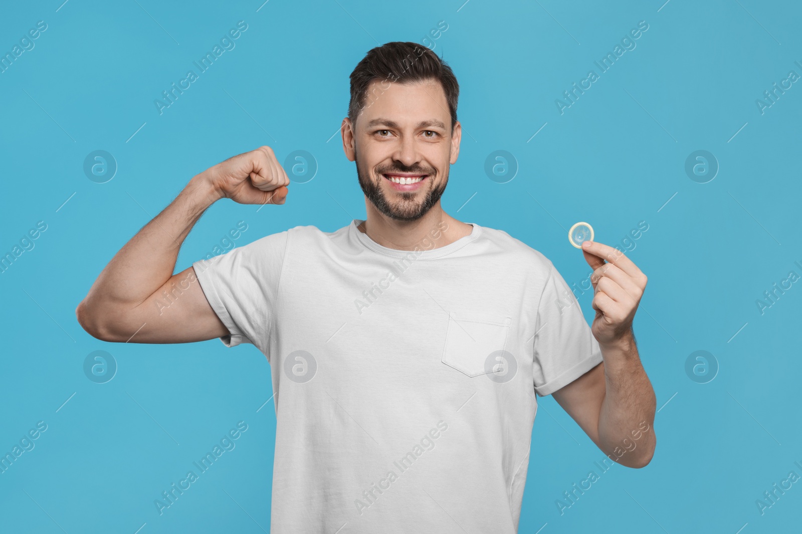 Photo of Happy man holding condom on light blue background