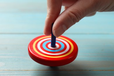 Woman playing with bright spinning top at light blue wooden table, closeup