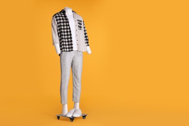 Photo of Male mannequin with sneakers dressed in white t-shirt, stylish checkered shirt and pants on orange background. Space for text
