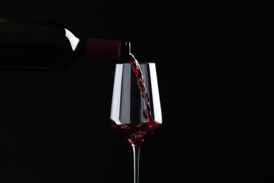 Pouring red wine from bottle into glass on black background