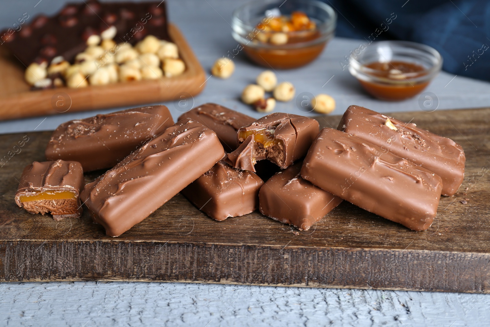 Photo of Delicious chocolate candy bars with caramel and nuts on grey wooden table